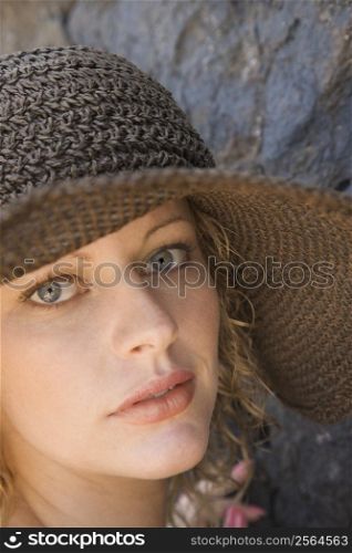 Close-up of young adult female Caucasian by rock wearing brimmed hat.
