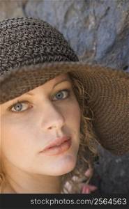 Close-up of young adult female Caucasian by rock wearing brimmed hat.