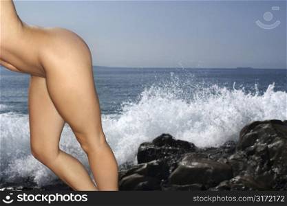 Close up of young adult female nude Caucasian leaning on rocky shore.