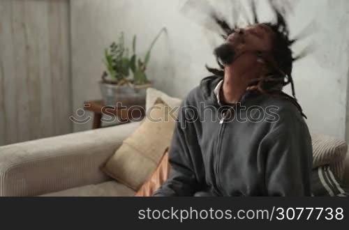 Close up of young african american man with dreadlocks putting on VR headset while sitting on the sofe in domestic interior. Excited man playing video games in virtual reality goggles. Slow motion.