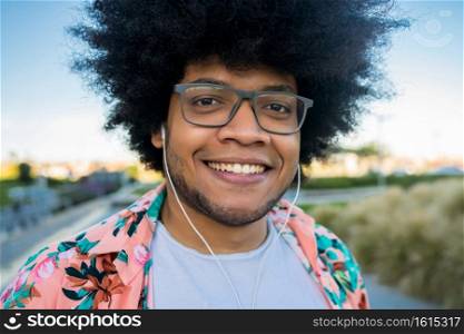 Close-up of young afro latin man smiling and looking at camera while standing outdoors on the street. Urban concept.