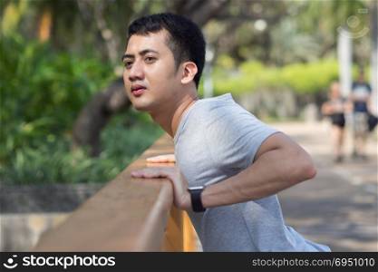 Close up of young asian man warm down to calm their body by stretching his body after exercising at the park in a warmlight afternoon. Young man exercise in the park. Outdoor exercise concept.