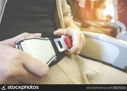 Close up of young asian woman hand passenger fastening seat belt while sitting on airplane for safety in safety on board with soft tone concept.