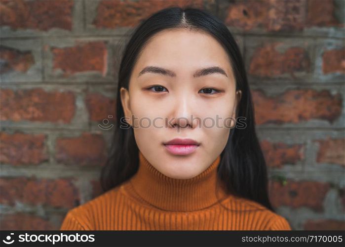 Close up of young beautiful Asian woman looking confident and standing against brick wall background.