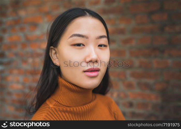 Close up of young beautiful Asian woman looking confident and standing against brick wall background.
