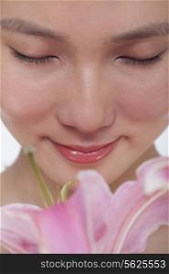 Close -Up of young beautiful woman smelling a large pink flower, studio shot