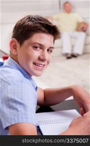 Close-up of young boy studying and looking at camera as father relaxes on the couch in the background