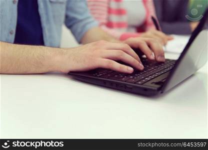 close up of young business man student student hands typing on laptop computer at modern school classroom, blured classmates in backgrond