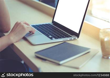 Close up of young businesswoman typing on computer laptop with blank screen at the office or cafe, business and mockup concept