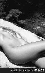 Close up of young Caucasian nude womans midsection lying on rock.
