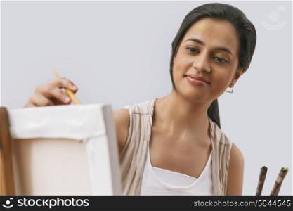 Close-up of young female artist painting on canvas isolated over gray background