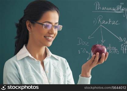 Close-up of young female teacher looking at apple against green board