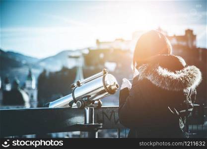 Close up of young girl using a tourist binocular in Salzburg, Old city and Fortress Hohensalzburg in the blurry background