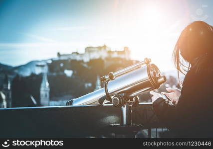 Close up of young girl using a tourist binocular in Salzburg, Old city and Fortress Hohensalzburg in the blurry background