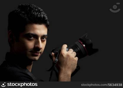 Close-up of young male photographer holding camera against black background