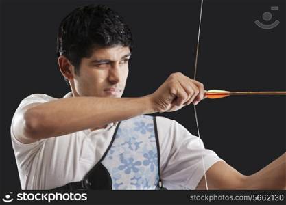 Close-up of young man aiming bow and arrow isolated over black background