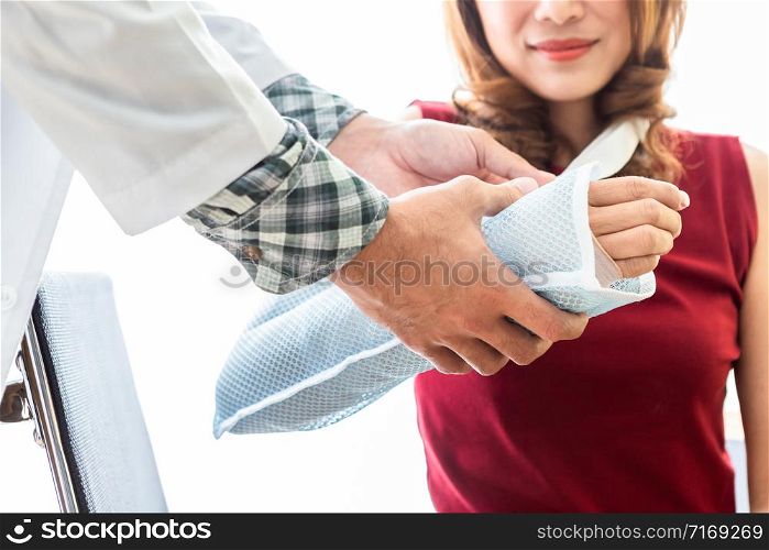 Close-up of Young man doctor of checking splint the arm of female patient hand due to with her arm broken for better healing sit in a wheelchair In the room hospital background.