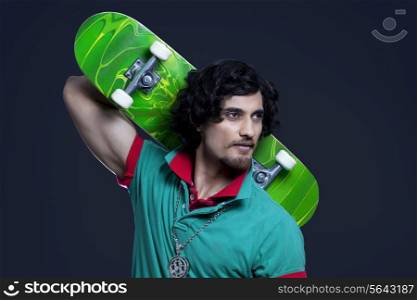 Close-up of young man holding skateboard behind head against black background