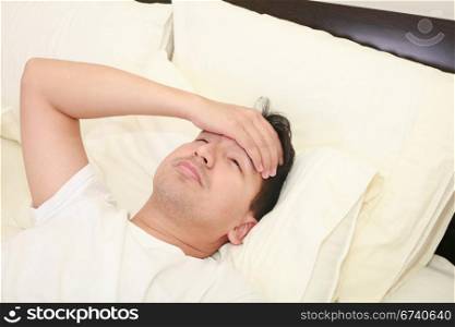 Close up of young man lying down in bed taking temperature and having flu
