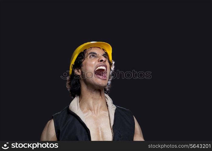 Close-up of young man with hardhat shouting against black background