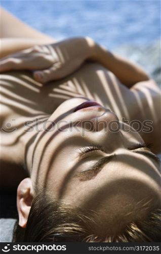 Close up of young nude multiethnic woman sunbathing on beach covered in shadow from palm tree.
