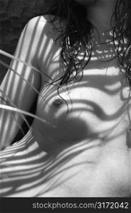 Close up of young nude woman covered in shadow from palm tree.