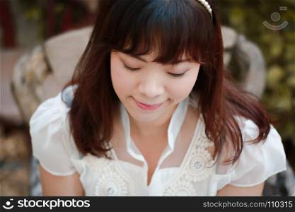 Close up of young pretty Asian woman in white dress with garden background.