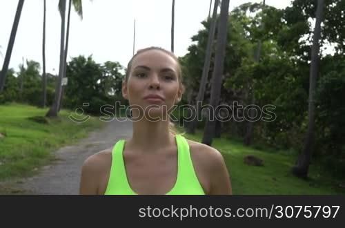 Close up of young pretty blonde female wearing exercise clothing running in tropical palm trees garden during beautiful summer day - video in slow motion