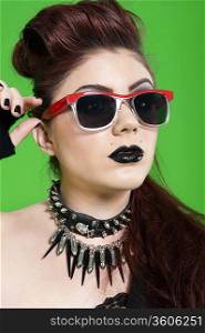 Close-up of young punk woman wearing sunglasses over green background