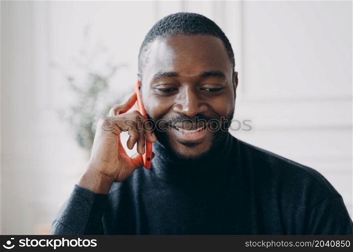 Close up of young smiling african man having business conversation on mobile phone while working in office, cheerful dark-skinned guy holding smartphone talking with friend or consulting client. Young smiling african man having business conversation on mobile phone