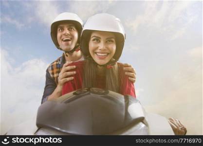 Close up of young smiling couple riding on a scooter.