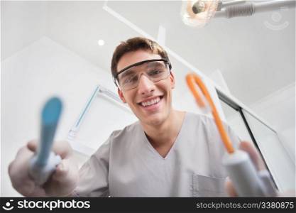 Close-up of young smiling dentist holding dental tools