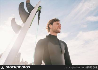 Close-up of young surfer standing at the beach next to his surfboard. Sport and water sport concept.