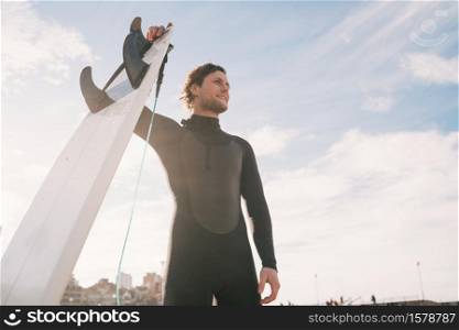 Close-up of young surfer standing at the beach with his surfboard and wearing black surfing suit. Sport and water sport concept.