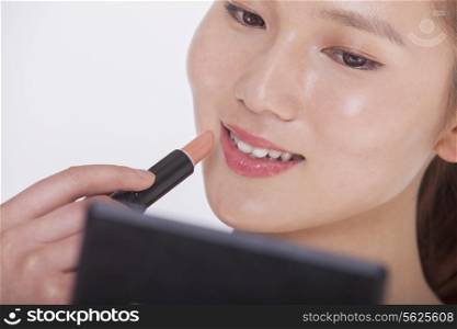 Close up of young woman applying lipstick in a mirror, studio shot