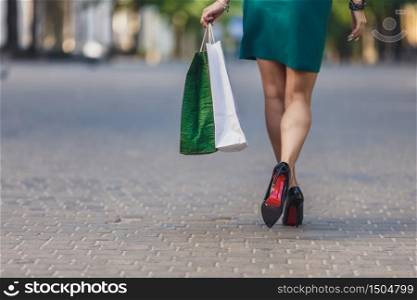 Close-up of young woman carrying shopping bags while walking along the street. Positive emotions and Shopping day concept.. Close-up of young woman carrying shopping bags while walking along the street. Woman sexy legs with handbag. Positive emotions and Shopping day concept.