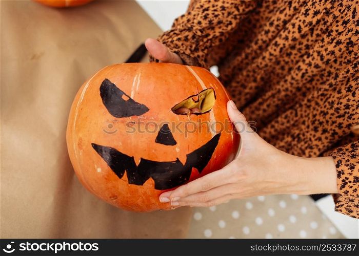 Close up of young woman carving Jack O Lattern from ripe orange pumpkin with knife on her wooden kitchen table. Female preparing all hallows eve Halloween party decorations. Background, copy space. Close up of young woman carving Jack O Lattern from ripe orange pumpkin with knife on her wooden kitchen table. Female preparing all hallows eve Halloween party decorations. Background, copy space.