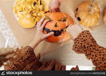Close up of young woman carving Jack O Lattern from ripe orange pumpkin with knife on her wooden kitchen table. Female preparing all hallows eve Halloween party decorations. Background, copy space. Close up of young woman carving Jack O Lattern from ripe orange pumpkin with knife on her wooden kitchen table. Female preparing all hallows eve Halloween party decorations. Background, copy space.