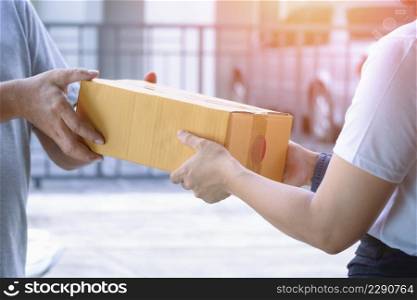 Close up of young woman hand receiving a parcel box from delivery man in front of home