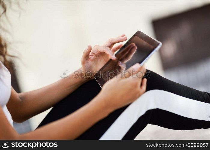 Close-up of young woman hands in sports clothes using digital tablet outdoors.