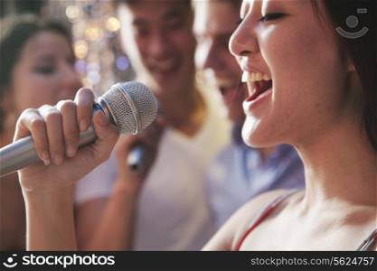 Close- up of young woman holding a microphone and singing at karaoke, friends singing in the background
