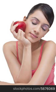 Close-up of young woman holding apple with eyes closed over white background