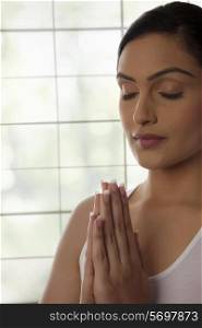 Close-up of young woman meditating with hands clasped against glass window