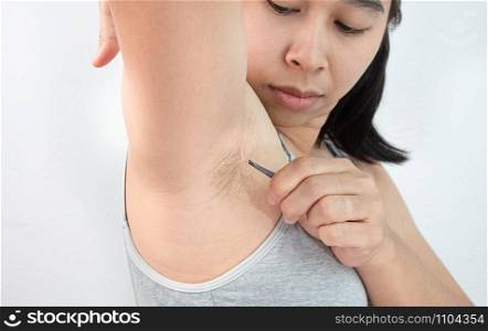 Close up of young woman plucking armpit underarm with tweezers isolated on grey background. Concept of Hygiene skin body care and beauty.