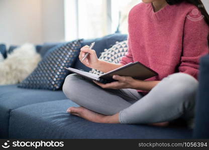 Close Up Of Young Woman Relaxing On Sofa At Home Writing In Journal