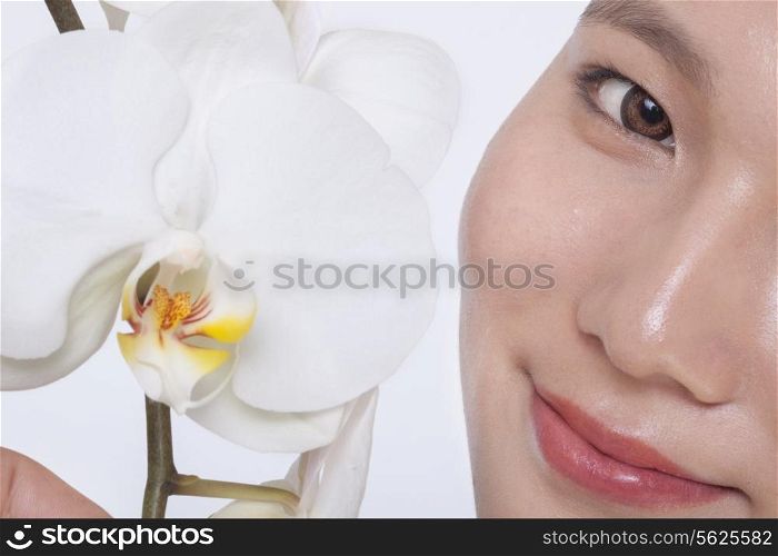 Close up of young woman smiling and a beautiful white flower, half face showing, studio shot