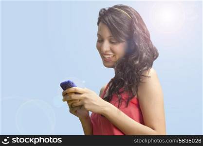 Close-up of young woman text messaging against sky