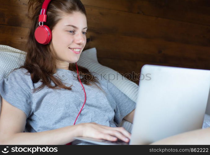 Close-up of young woman using laptop and headphones in a comfortable bed at home.