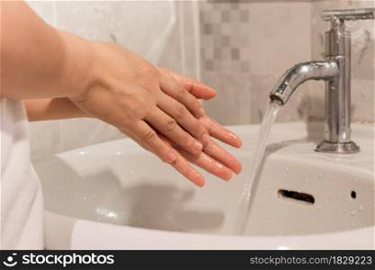 Close-up of young woman washing hands over sink in bathroom at home. hygiene treatment concept