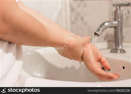 Close-up of young woman washing hands over sink in bathroom at home. hygiene treatment concept